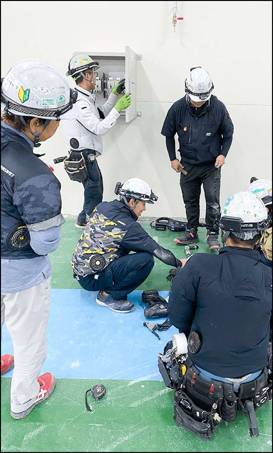 ヘルメット姿の作業員たちが電気設備の点検や工具を使った作業を行っている様子